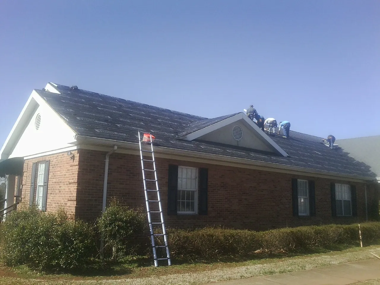 Crew tearing shingles off a brick ranch roof with a ladder set — Emergency Roof Repair work by our crew in Dalton